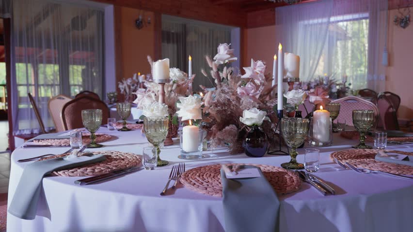 Beautifully arranged wedding reception table with floral centerpieces, candlelight, and delicate glassware. Soft lighting adds a romantic ambiance to this exquisite setup.