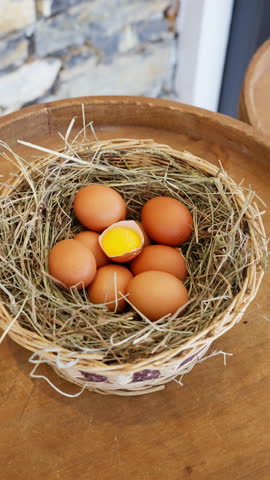 Farm fresh eggs in straw nest close up vertical format, brown organic eggs with cracked yolk and natural protein food.