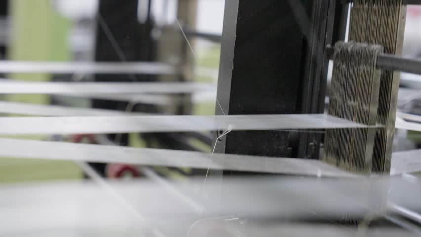 Close-up of a loom machine in action, showcasing threads, moving parts, and the weaving process, ideal for textile manufacturing, craftsmanship, industrial production, and machinery visuals.