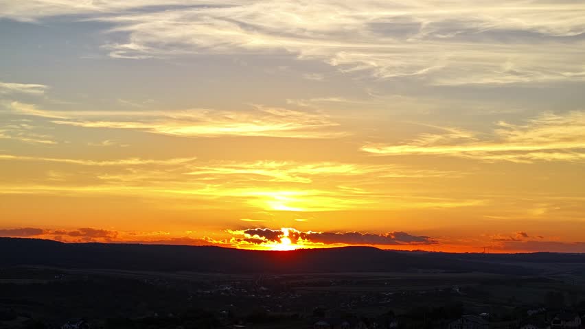 Aerial hyper lapse of fiery sunset, glowing golden sun hiding behind the hill - Botosani, Romania