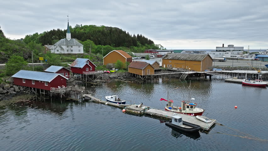 Drone view of harbor and church in Lofoten Islands, Norway. Scenic norwegian fishing village with rorbu cabins along calm Arctic waterfront.
