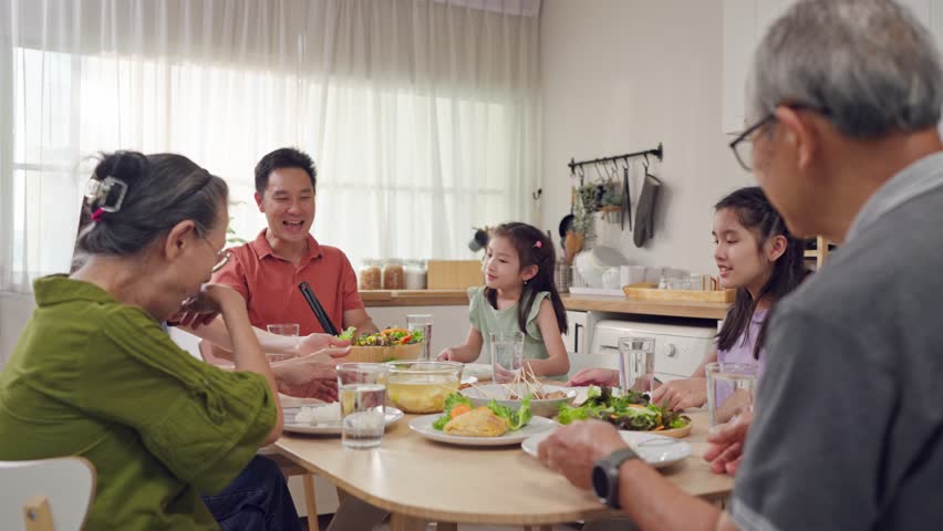 Asian loving family spending quality time, having dinner in cozy house. Grandparents, parents and daughter having fun, eating food, celebrate weekend reunion gathered together at dining table at home.