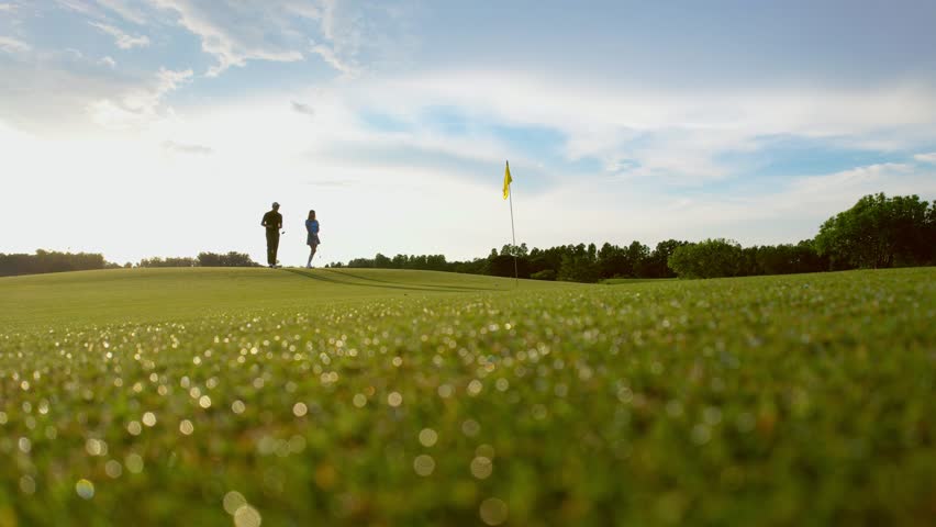 Drone view of young golfers swing clubs together on a scenic golf course. Attractive man and woman enjoy outdoor recreation with light exercise and sport lifestyle while playing golf at course ground.