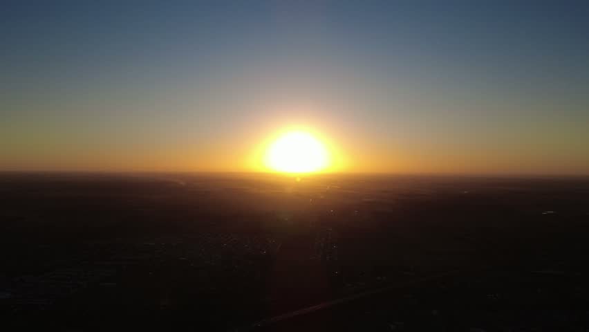 Majestic round sun setting over highway and green fields seen from a high drone perspective.