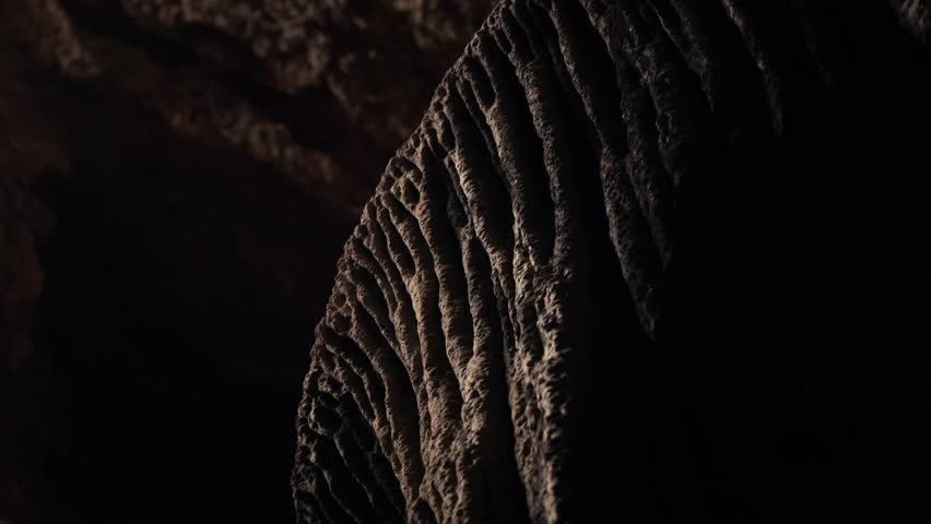 Close up of limestone cave formation in Ibiza showing textured stalactite surface illuminated by low natural light creating dramatic shadows.