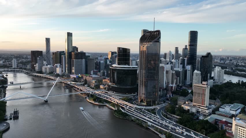 Slow drone tracking along the Brisbane River at golden hour, moving past Queens Wharf and The Star Brisbane toward the CBD skyline and Neville Bonner Bridge, Brisbane, QLD, Australia
