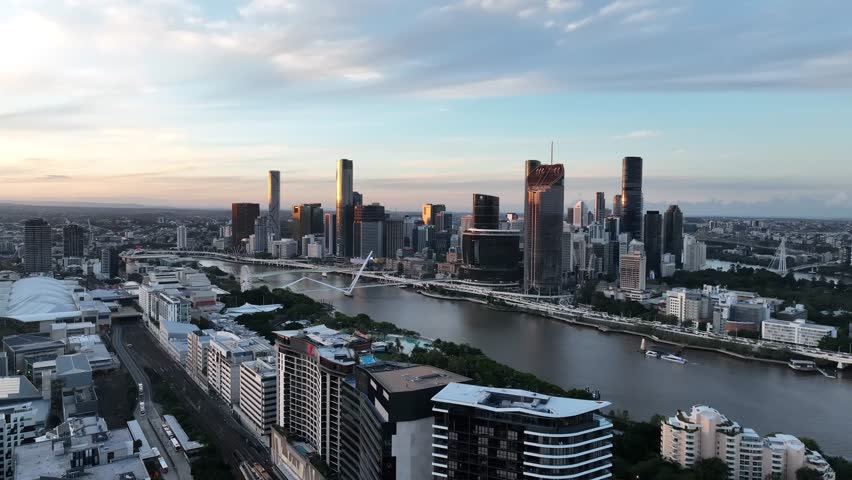 Slow drone side tracking at golden hour, keeping the Emporium Hotel rooftop in the foreground with the Brisbane River, Queens Wharf and the CBD skyline beyond, Brisbane, QLD, Australia