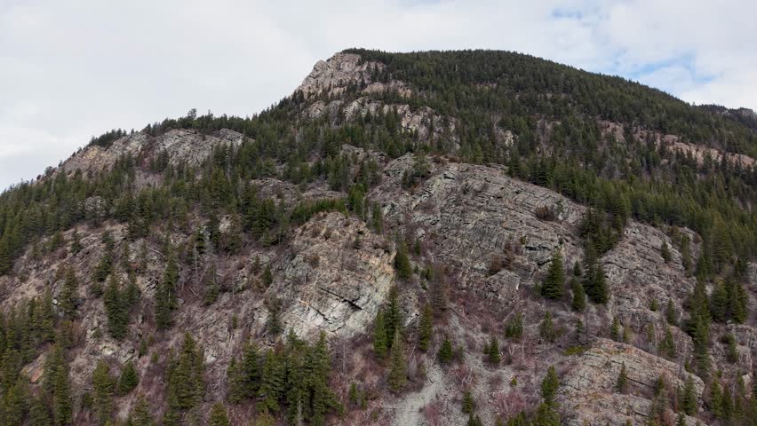 An aerial drone shot of a rugged rocky mountain ridge with evergreen pine trees in wilderness near Whitefish Montana and the Flathead River