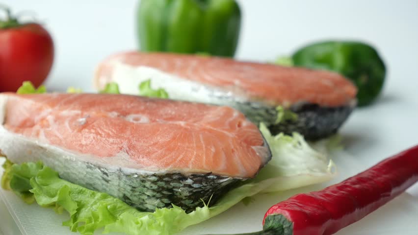 Fresh raw salmon steaks on lettuce with vibrant vegetables and green peas in a professional kitchen setting