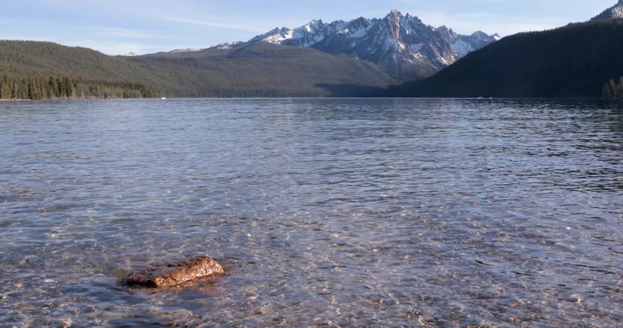 A large body of water with mountains in the background. The water is calm and clear. A rock is floating in the water at redfish lake near stanley idaho