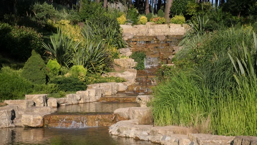 Artificial waterfall cascading down stone levels in lush green park garden during sunset