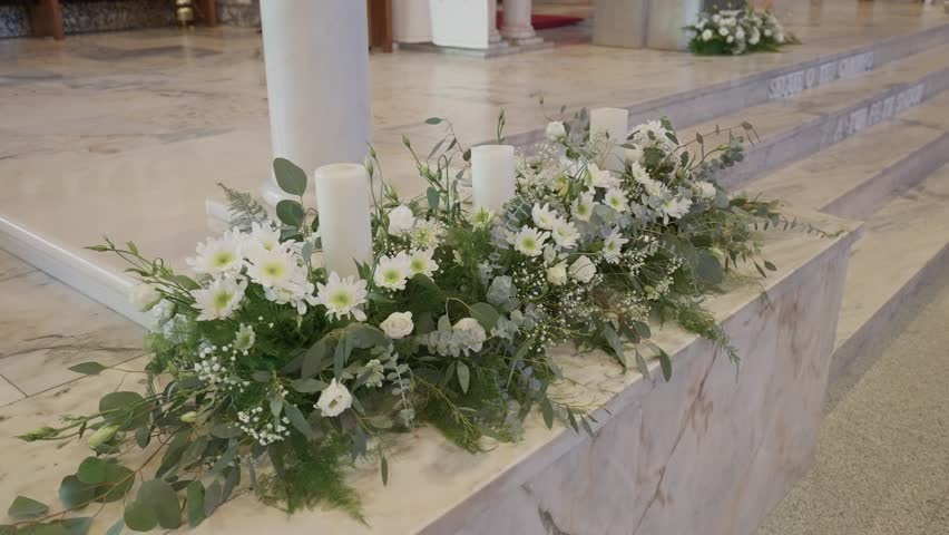 Elegant white flowers and candles decorating church steps for baptism or wedding ceremony, creating a calm sacred atmosphere indoors