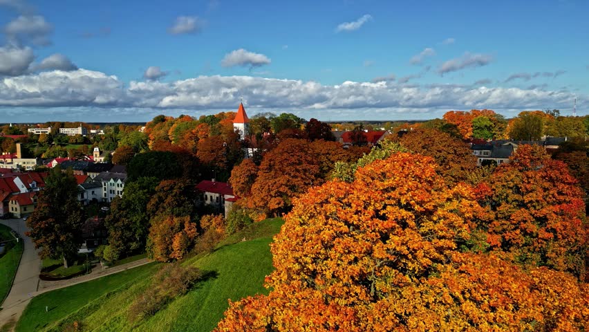 Colorful autumn foliage surrounding small town with red roofed church and rolling green hillside under blue sky