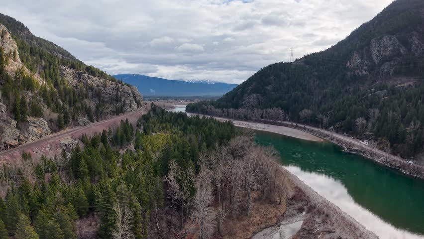 Aerial view of a winding river with turquoise water flowing between forested mountains and rocky cliffs in a remote valley near Whitefish, Montana