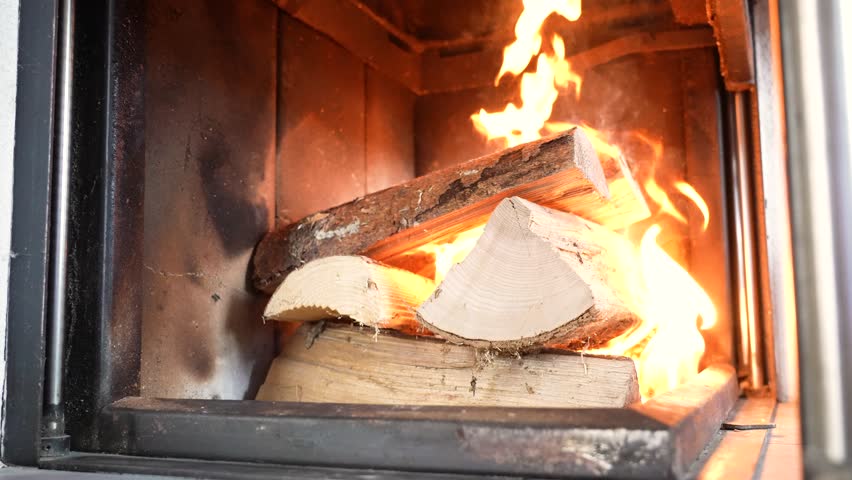 Close view of burning firewood inside a fireplace with bright orange flames. Cozy indoor scene capturing warmth, comfort and natural fire movement in a home setting.