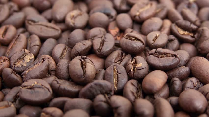 A detailed, macro view shows a pile of coffee beans. Various shades of brown are visible. The beans have different sizes and shapes. Subtle surface textures can be easily seen.
