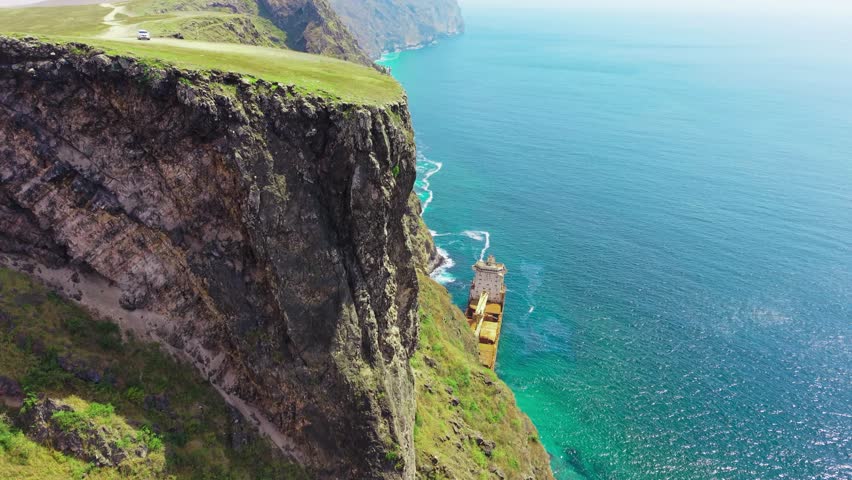 Aerial view of a group of young men and women standing on a high cliff above the Jernas shipwreck by the sea in Salalah, Oman.