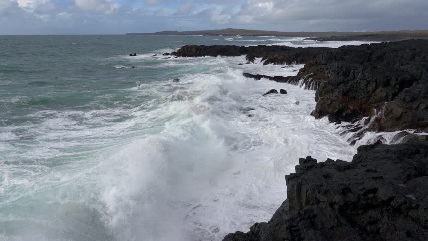 A dramatic coastal scene where powerful waves slam into rocky shores, sending mist into the air and revealing the untamed beauty of Iceland’s rugged ocean frontier