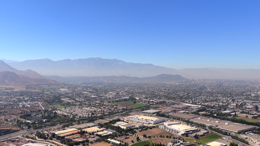 Santiago, Chile during a clear morning. The frame shows the urban city landscape surrounded by the high Andes mountain range and a clear horizon. High altitude right tracking aerial shot.