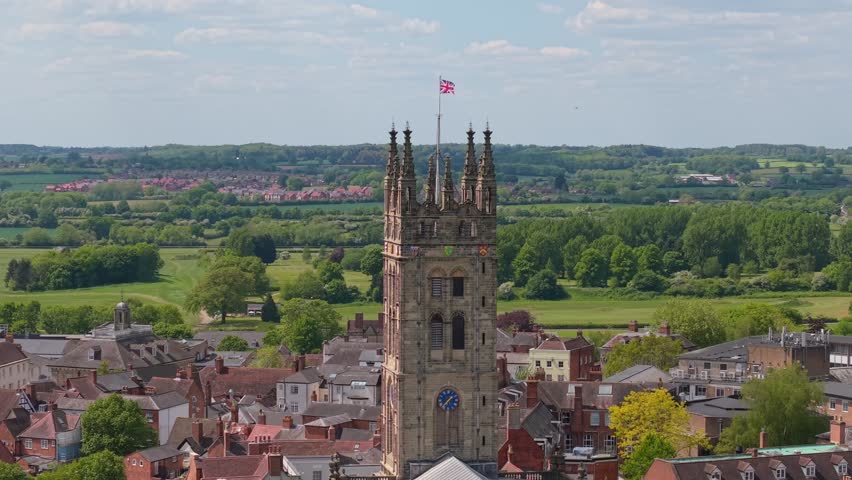 Orbiting footage of St Mary’s Church belfry in Warwick with the England flag waving at the top, revealing the surrounding historic town and village scenery.