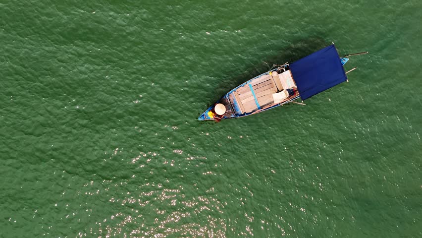 Fisherman casting a traditional net into the river from a wooden boat, aerial top down view, hoi an, Vietnam.
