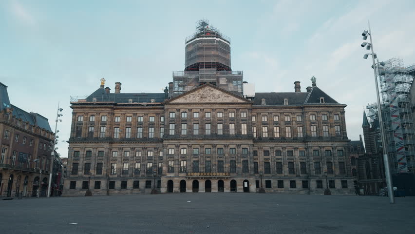 Royal Palace of Amsterdam on an empty Dam Square during an early morning, with the central tower covered in restoration scaffolding