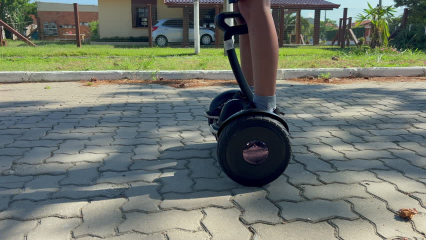 Child rides hoverboard along residential street on brick pavement, side follow tracking shot with legs and shoes in frame, daylight outdoor mobility, slow motion 4K60.