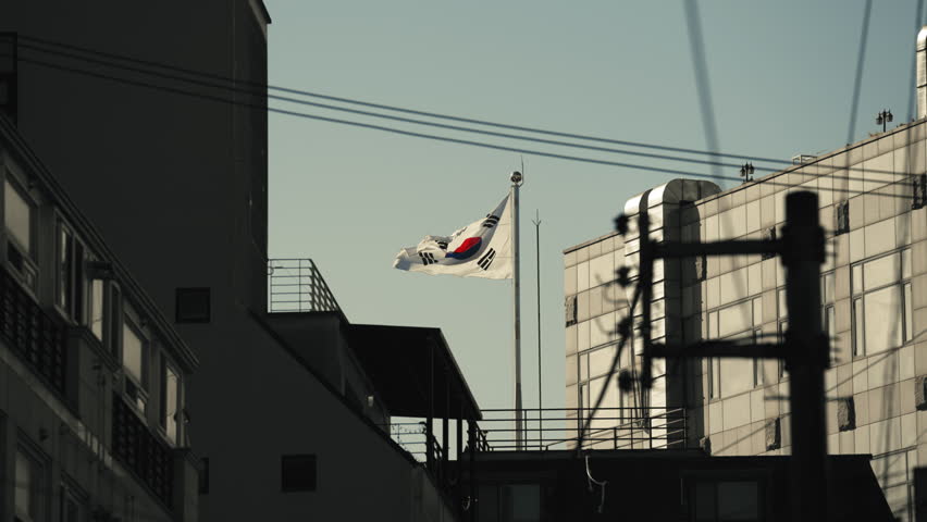 South Korean flag waving in slow motion above city buildings with power lines in Seoul South Korea