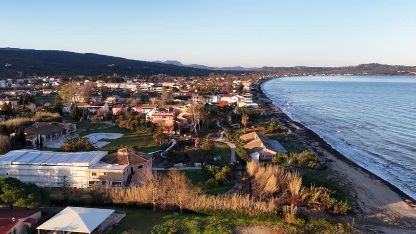 Aerial View of a Beautiful Coastal Village and Beach in Corfu Greece, Gentle Ocean Waves Crashing on the Shoreline at Sunrise, Seaside Resort Landscape