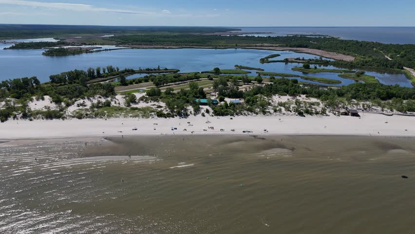 Aerial from far over Lake Winnipeg looking east at Grand Beach, Manitoba. Summer day with people on the beach, sandy shoreline, lagoon, and boreal forest in the background.