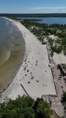 Aerial drone vertical footage from far over Lake Winnipeg looking east at Grand Beach, Manitoba. Summer day with people on the beach, sandy shoreline, lagoon, and boreal forest in the background.
