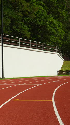 A fit female athlete in black sportswear sprints along a red running track at an outdoor stadium during a sunny day.
