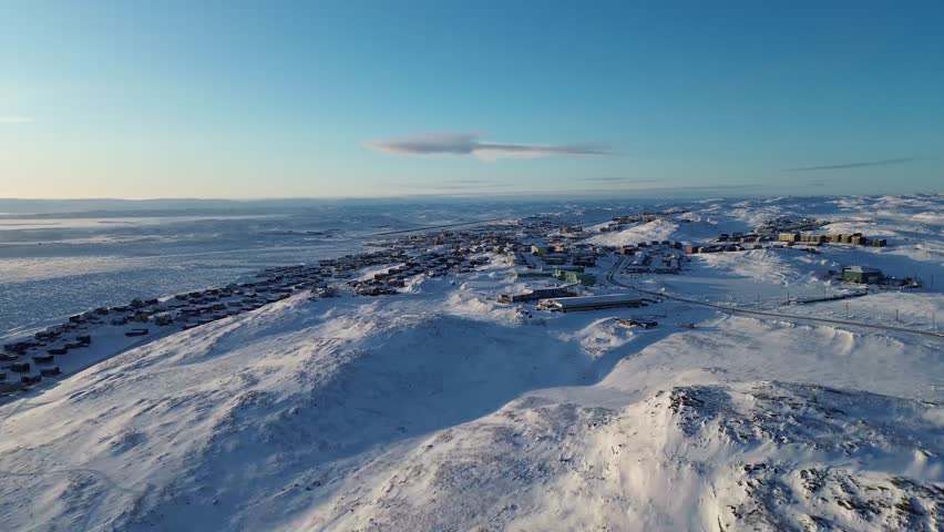 Cinematic drone flight pushing toward the city of Iqaluit, Nunavut, showcasing the unique Arctic capital and infrastructure amidst a vast, frozen winter landscape.