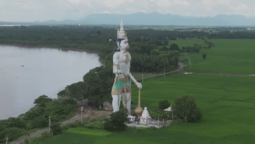 Aerial drone view of a giant Hanuman statue and temple beside a wide river, paddy fields, Srikakulam, Andhra Pradesh, India.