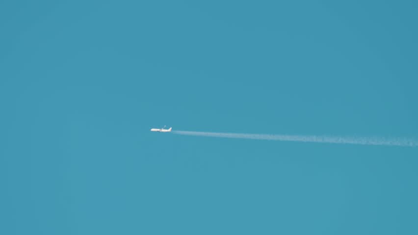 Cargo aircraft flying through clear blue sky at high altitude. Freight airplane leaving thin vapor trail stretching across atmosphere. Heavy transport airliner moving above clouds creating minimal