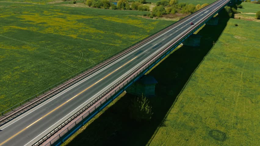 White wagon car driving by bridge in picturesque country scene. White station vehicle moving across elevated road in scenic rural landscape. Compact white auto passing over countryside viaduct