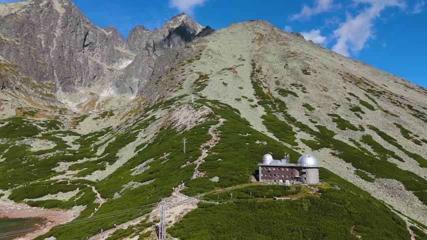 Drone panning toward Skalnaté Pleso Observatory in High Tatras Slovakia revealing astronomical dome beneath dramatic alpine mountain peaks.