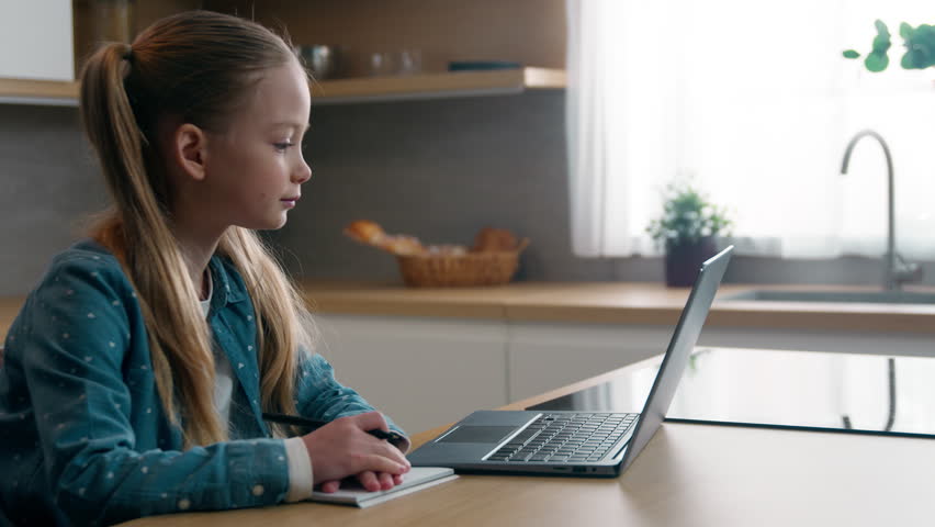 Home schooling quarantine e-learning at home kitchen concept. Caucasian kid child school girl daughter exams learn studying using laptop writing listen online teacher study watching course lesson