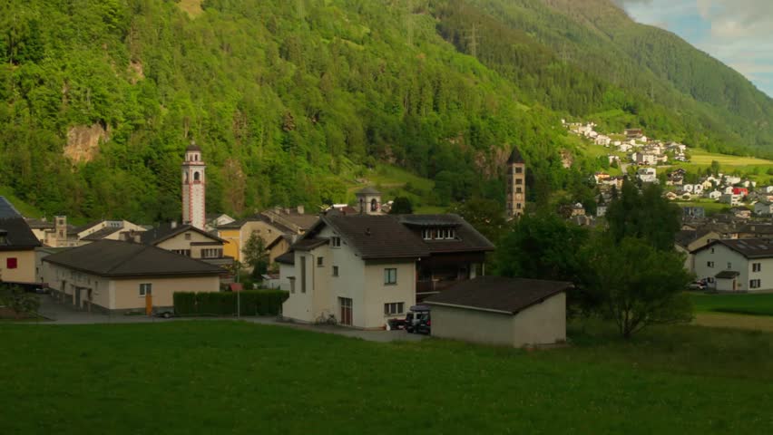 Panoramic view of Poschiavo village with church towers nestled in green alpine valley. Beautiful Swiss mountain landscape features traditional architecture and summer scenery.