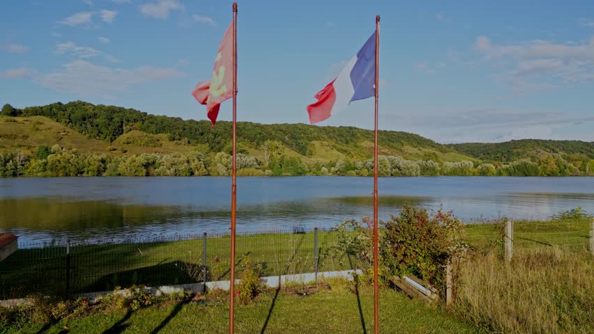 Drone footage flies between flags of Normandy and France to reveal beauty of rural countryside landscape scene with river Seine on sunny summer day at golden hour