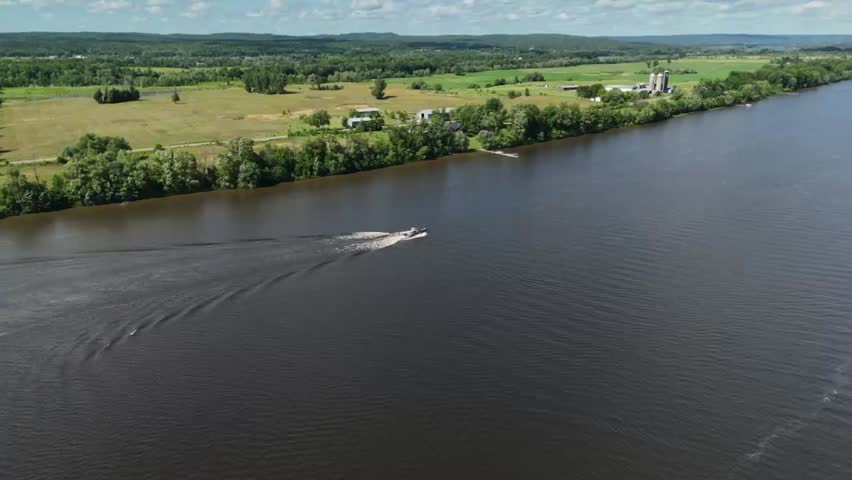 A boat cruises across the water, with a wakeboarder riding behind.  The camera then pans up, revealing a stunning summer landscape.  