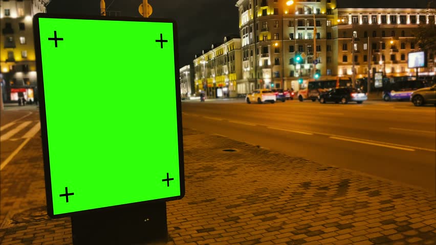 Green screen mockup concept. Nighttime shooting of an evening city street with a billboard on a green screen with tracking markers to add custom digital advertising or promotional content. 4k footage