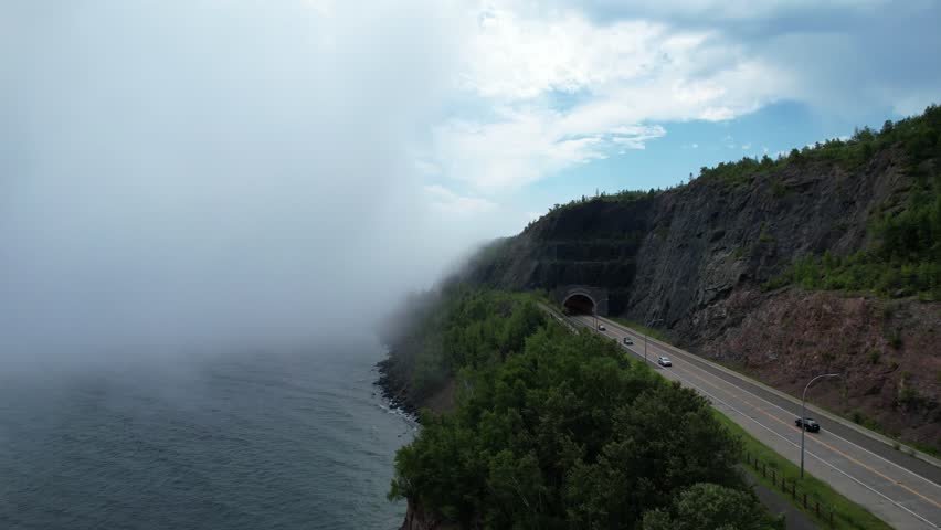 Aerial of North Shore Minnesota tunnel on the coast of Lake Superior with low fog. Push shot along shore and highway approaching the tunnel.
