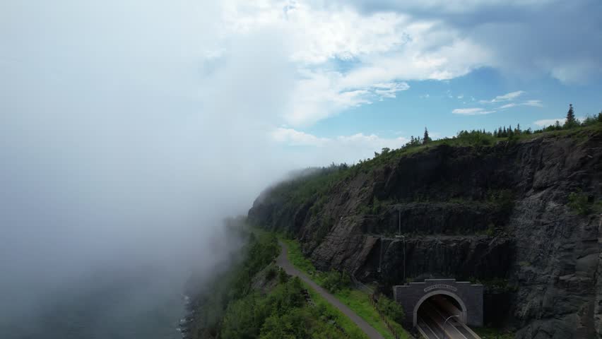 Aerial of North Shore Minnesota tunnel on the coast of Lake Superior with low fog.  Rising drone shot above cliff and clouds.