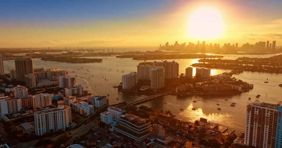 Golden hour in Brickell Key in Miami, Florida, USA. Biscayne Bay waterscape reflects the orange light. Multiple vessels are on the water. Aerial view.