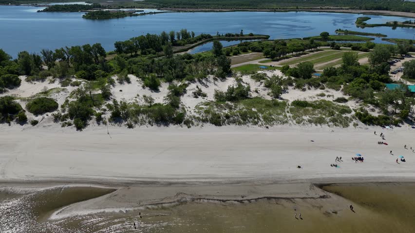 Aerial drone footage from far over Lake Winnipeg looking east at Grand Beach, Manitoba. Summer day with people on the beach, sandy shoreline, lagoon, and boreal forest in the background.
