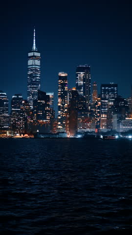 Iconic modern luminous skyline of New York, USA. Night scenery of the city from the river. Vertical video.