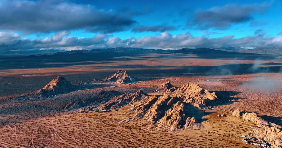 Approaching the rocks surrounded by the cars and campervans of the tourists. Fluffy clouds float in the sky and throw the shadows on the desert. Joshua Tree National Park, California, USA.