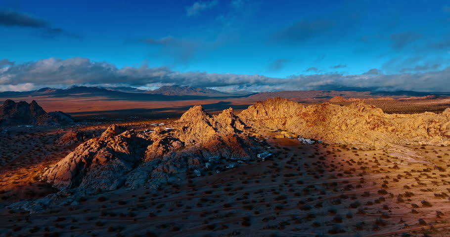 Lots of campervans stand around the rocks in the desert covered with shrubs. Beautiful scenery of Joshua Tree National Park, California, USA at the time of sunset.