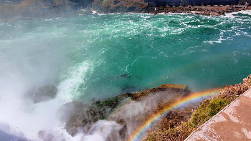 Over the dangerous shore of Niagara Falls. Spraying water create beautiful rainbow. Sightseeing stunning landmark on sunny day.